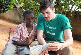 Vrijwilligerswerk in Togo:Een vrijwilliger in Togo helpt een scholier bij het lezen van een Engelstalig boek tijdens de groepsreis voor jongeren. Een vrijwilliger in Togo helpt een scholier bij het lezen van een Engelstalig boek tijdens de groepsreis voor jongeren.